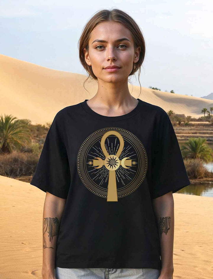 Junge Frau trägt das schwarze „Ankh des ewigen Lichts“ Damen Relaxed Shirt  vor einer sandigen Kulisse.
