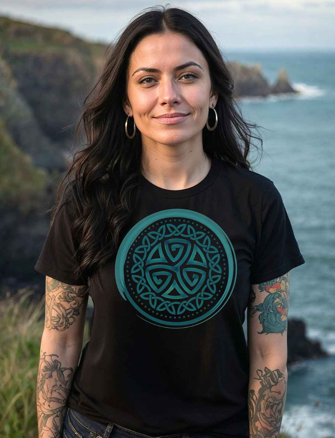 Model trägt das Triskele der Elemente Damen Organic Shirt in Schwarz mit türkisfarbenem Symbol vor atlantischer Steilküste.