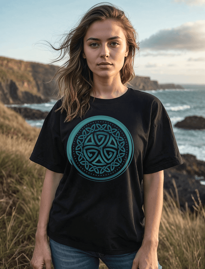 Model trägt das schwarze Aqua Triskele Unisex Bio-Shirt in Oversized-Passform vor maritimer Kulisse bei Sonnenuntergang.