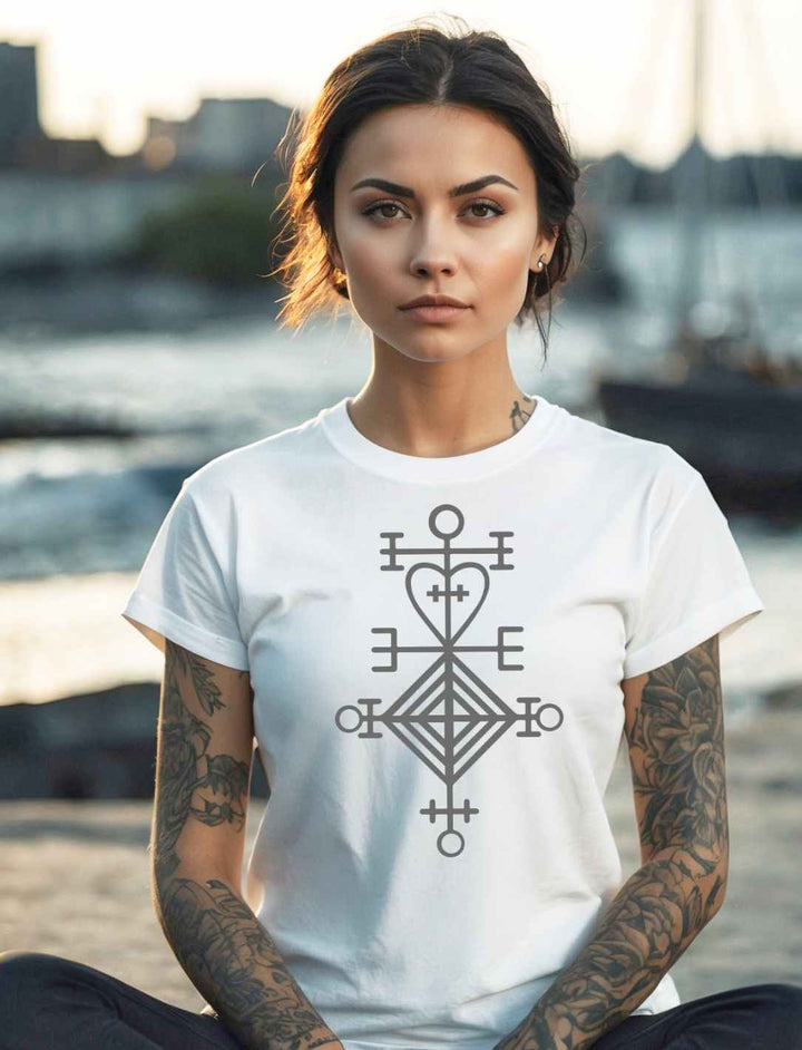 Junge Frau trägt ein weisses Astarstafur Damen T-Shirt mit isländischen Symbol für Liebe und Schutz, am Hafen sitzend – kraftvolles Design, inspiriert von nordischer Tradition.