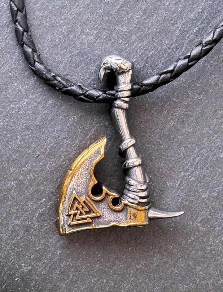 Edelstahlanhänger in Form einer nordischen Axt mit Valknut-Symbol, inszeniert auf schwarzem Schiefer und geflochtenem Lederband