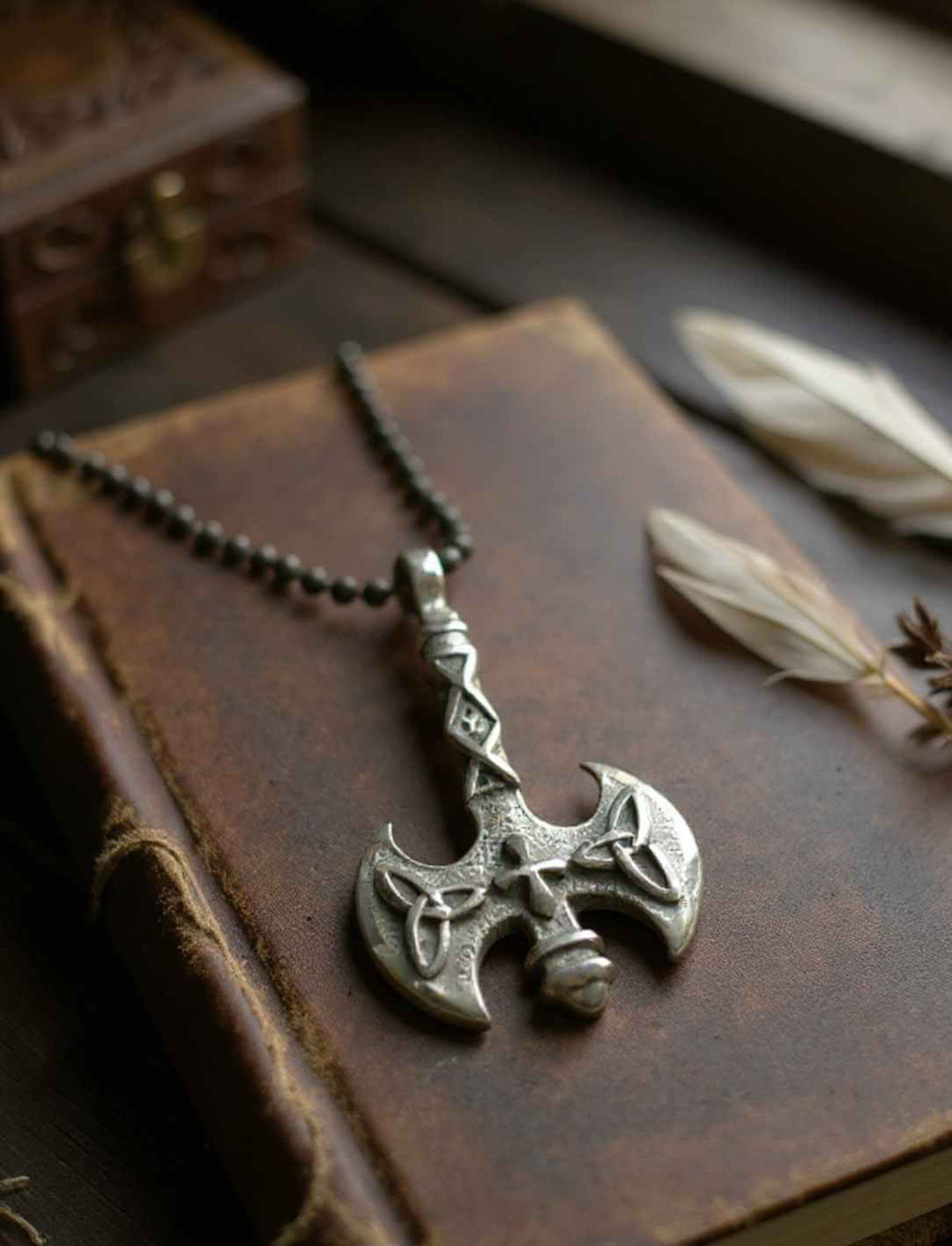 Anhänger „Axt des Sonnenkreuzes“ aus Edelstahl, inszeniert auf Buch mit Feder und geheimnisvollem Licht an Edelstahlkette in schwarz.