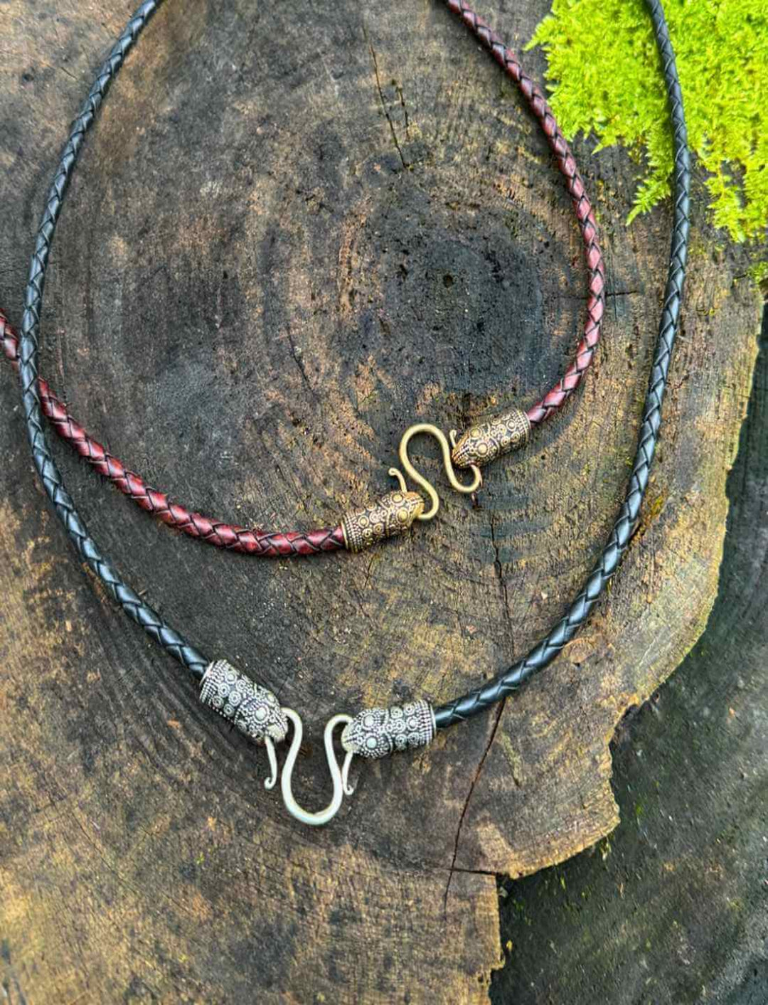 Beide Varianten des 'Band des Rabenwächters', schwarz/silber und braun/bronze, präsentiert vor einem Waldhintergrund.