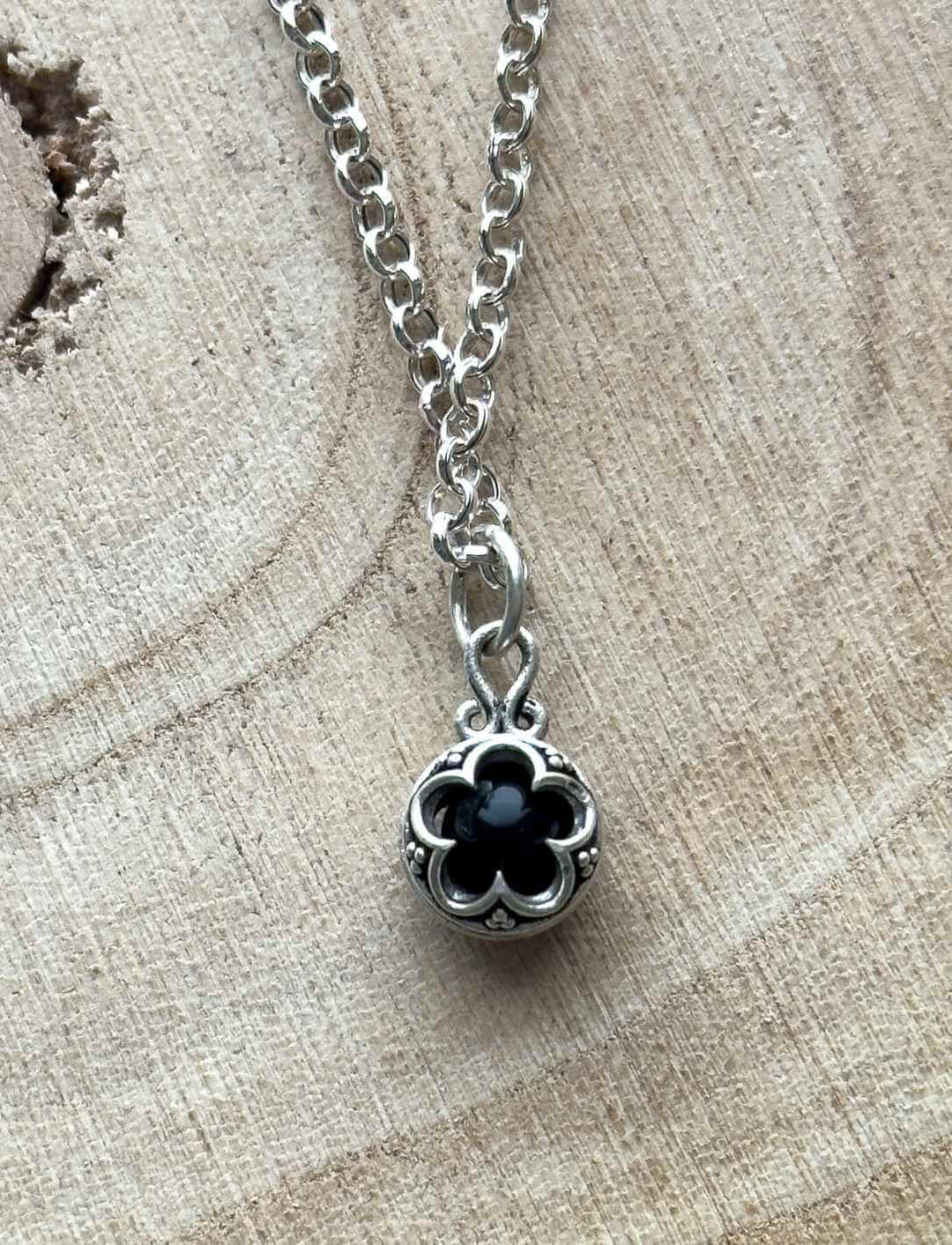 Blüte von Gotland – Silberamulett mit Onyx in schwarz,  inspiriert von Gotland-Ornamenten auf hellem Tisch mit Silberkette.