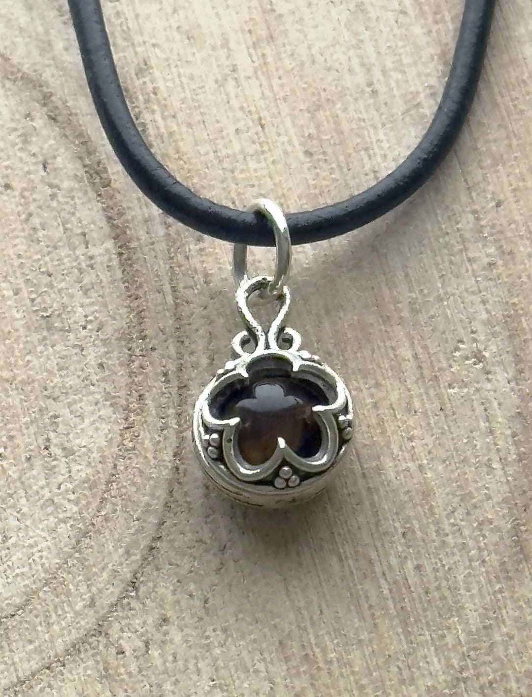 Blüte von Gotland – Silberanhänger mit dunkelbraunem Tigerauge auf heller Holzoberfläche an Lederband.