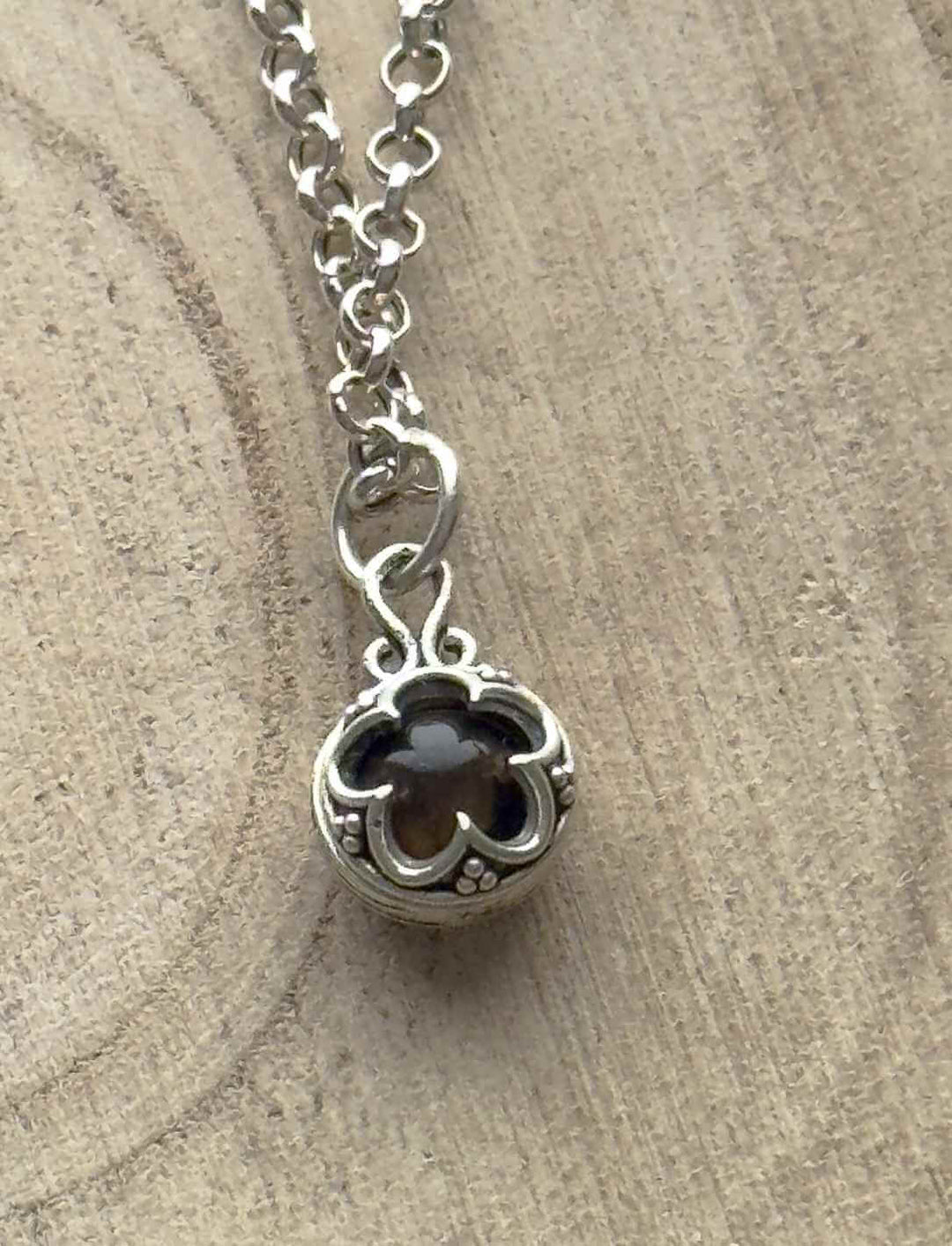 Silberamulett Blüte von Gotland mit dunkelbraunem Tigerauge, getragen an feiner Kette aus 925 Sterling Silber.