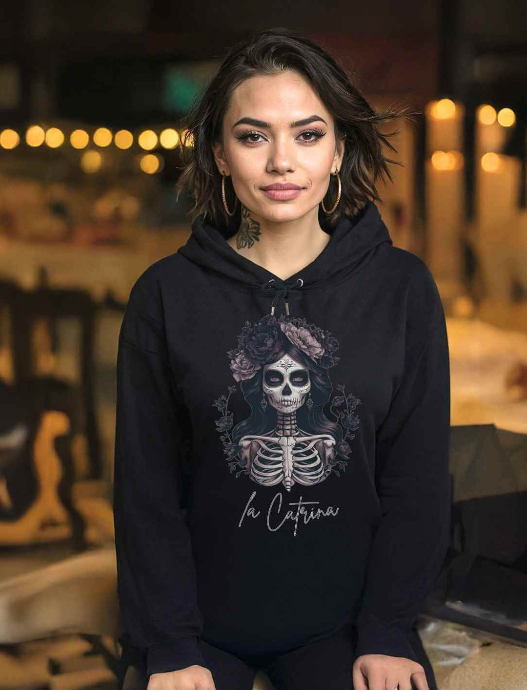 Frau in einem schwarzen Catrina Deluxe Unisex Hoodie – Ausdrucksstarke Día de los Muertos Kunst, die die Schönheit mexikanischer Tradition mit Eleganz und Mystik verbindet.