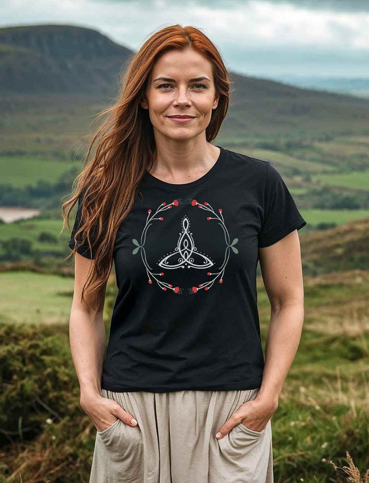 Frau mit langen roten Haaren trĂ€gt das âCeltic Motherâ Bio-Shirt in Schwarz vor einer grĂŒnen Landschaft.