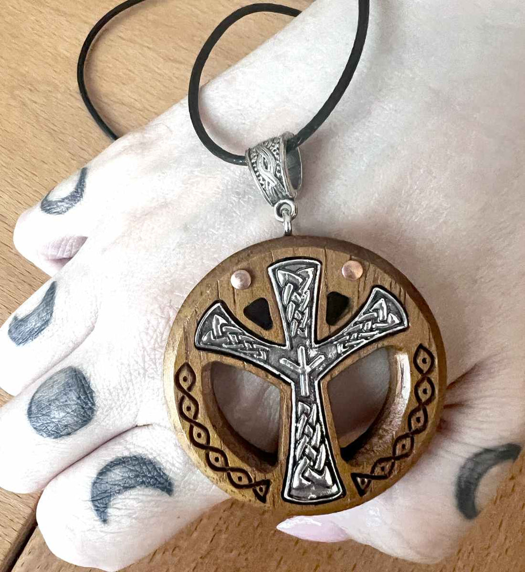 Hand hält die detailreiche keltische Kreuz Halskette mit nordischem Algaiz Rune Akzent