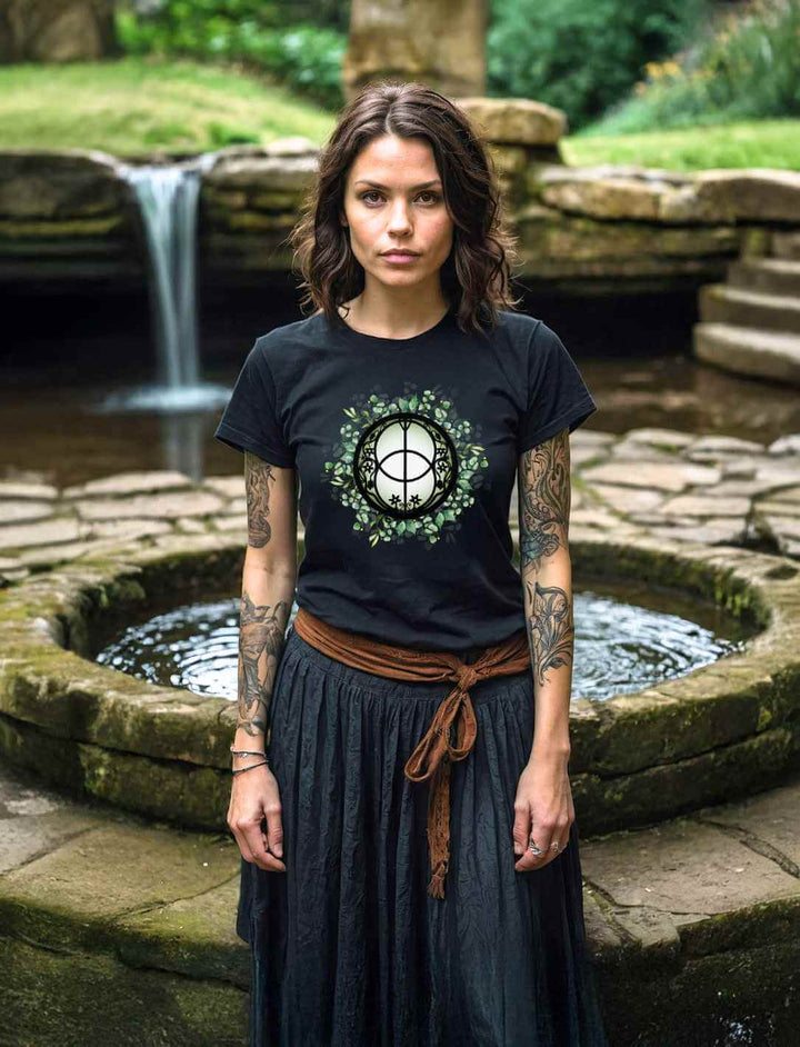 Model trägt das schwarze Chalice Well T-Shirt vor einem Brunnen – inspiriert von der heiligen Quelle in Glastonbury, Symbol für Heilung, Weisheit und spirituelle Erneuerung