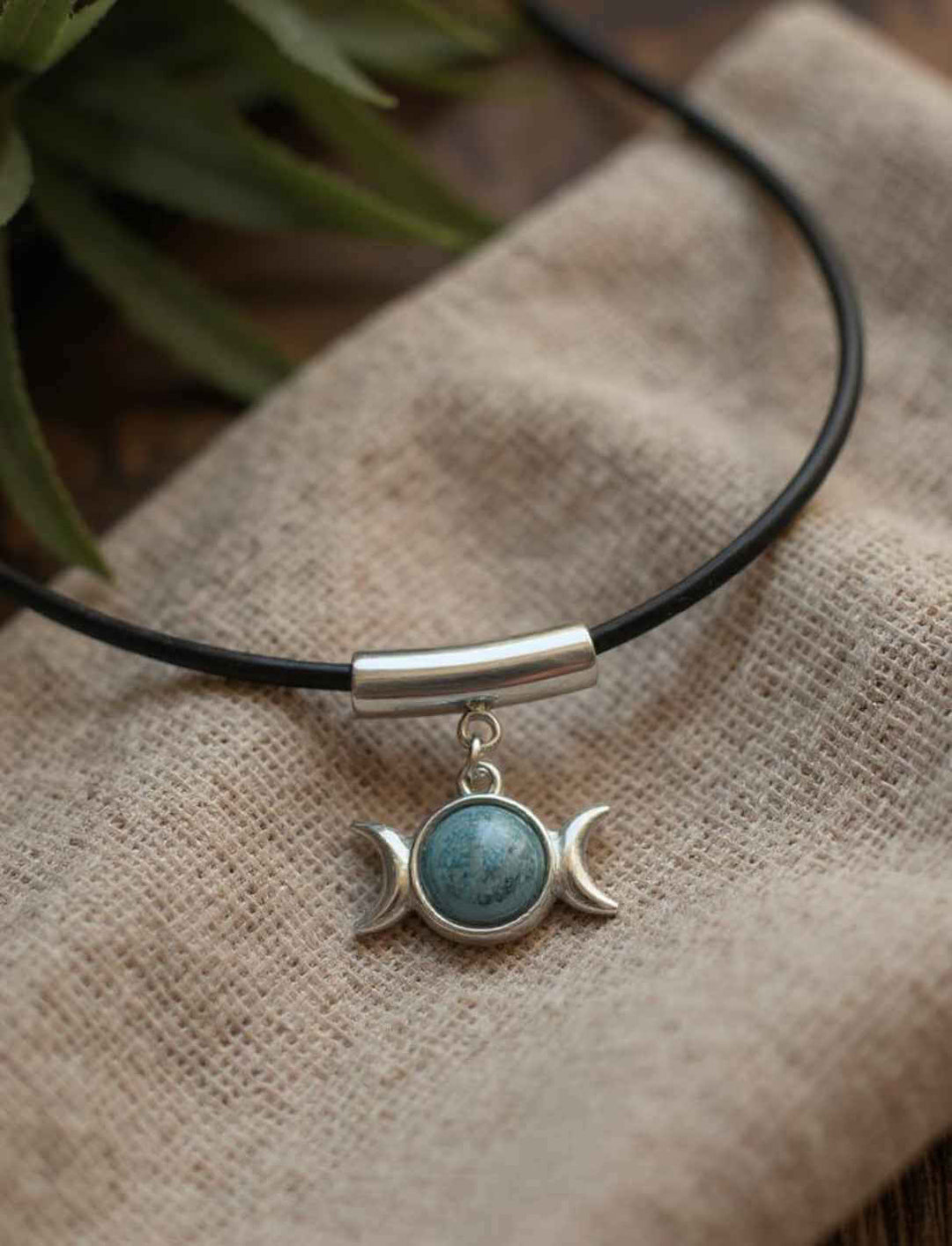 Dreimondzirkel Edelstahlanhänger mit Apatit-Stein auf Lederkette, liegend auf beigem Leinentuch