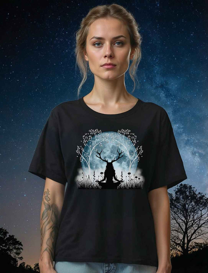 Model trägt das Damen Relaxed T-Shirt „Druidin der silbernen Wälder“ in Schwarz vor einem nächtlichen Waldhintergrund. Das Design zeigt eine Druidin unter einem leuchtenden Lebensbaum im Mondlicht.