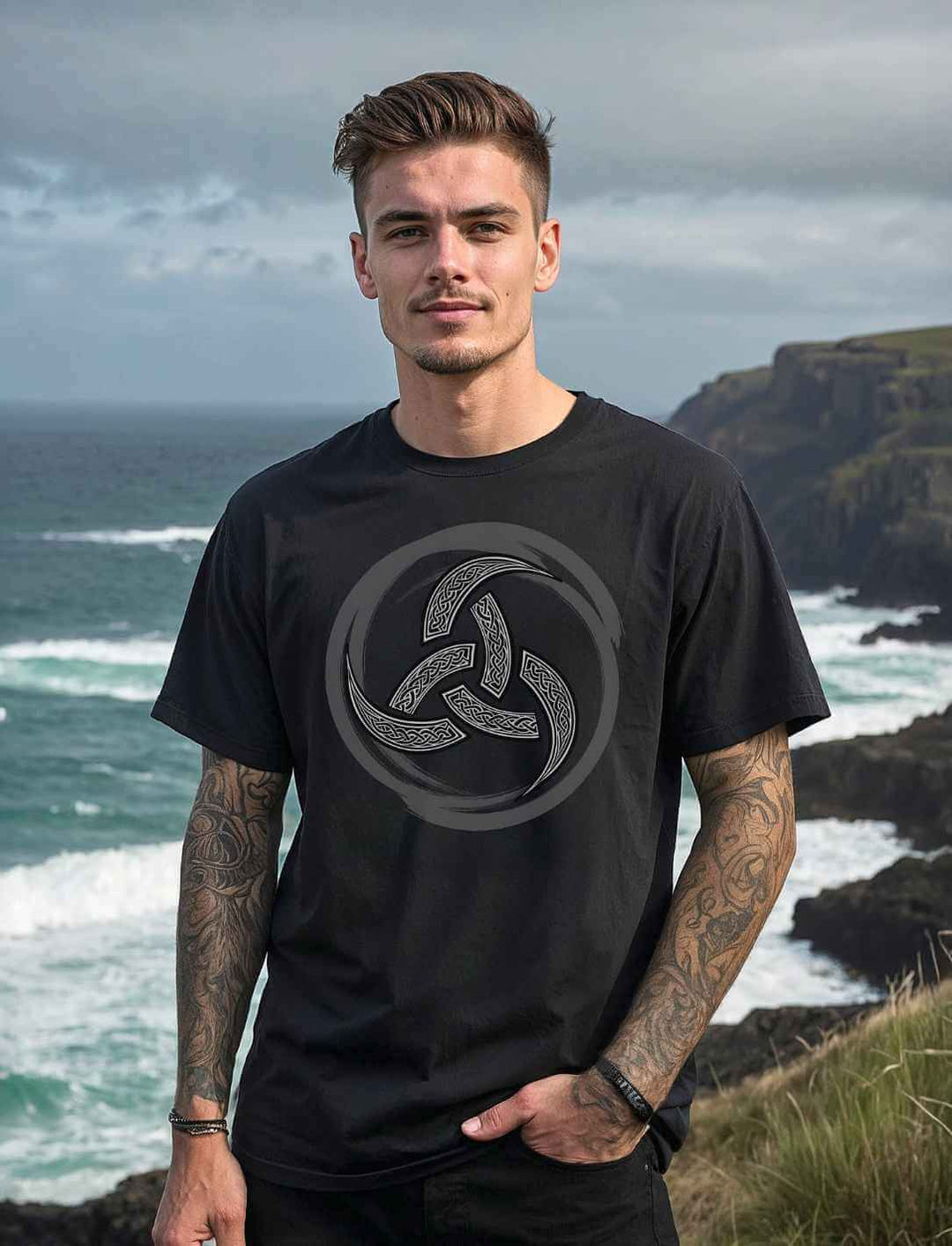 Männliches Model trägt das schwarze Oversized T-Shirt mit keltischer Triquetra in rauer Landschaft am Meer.
