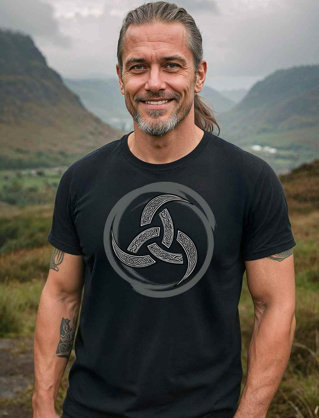 Mann trägt schwarzes Runental T-Shirt mit silbernem Triquetra-Symbol vor nebeliger Hügellandschaft