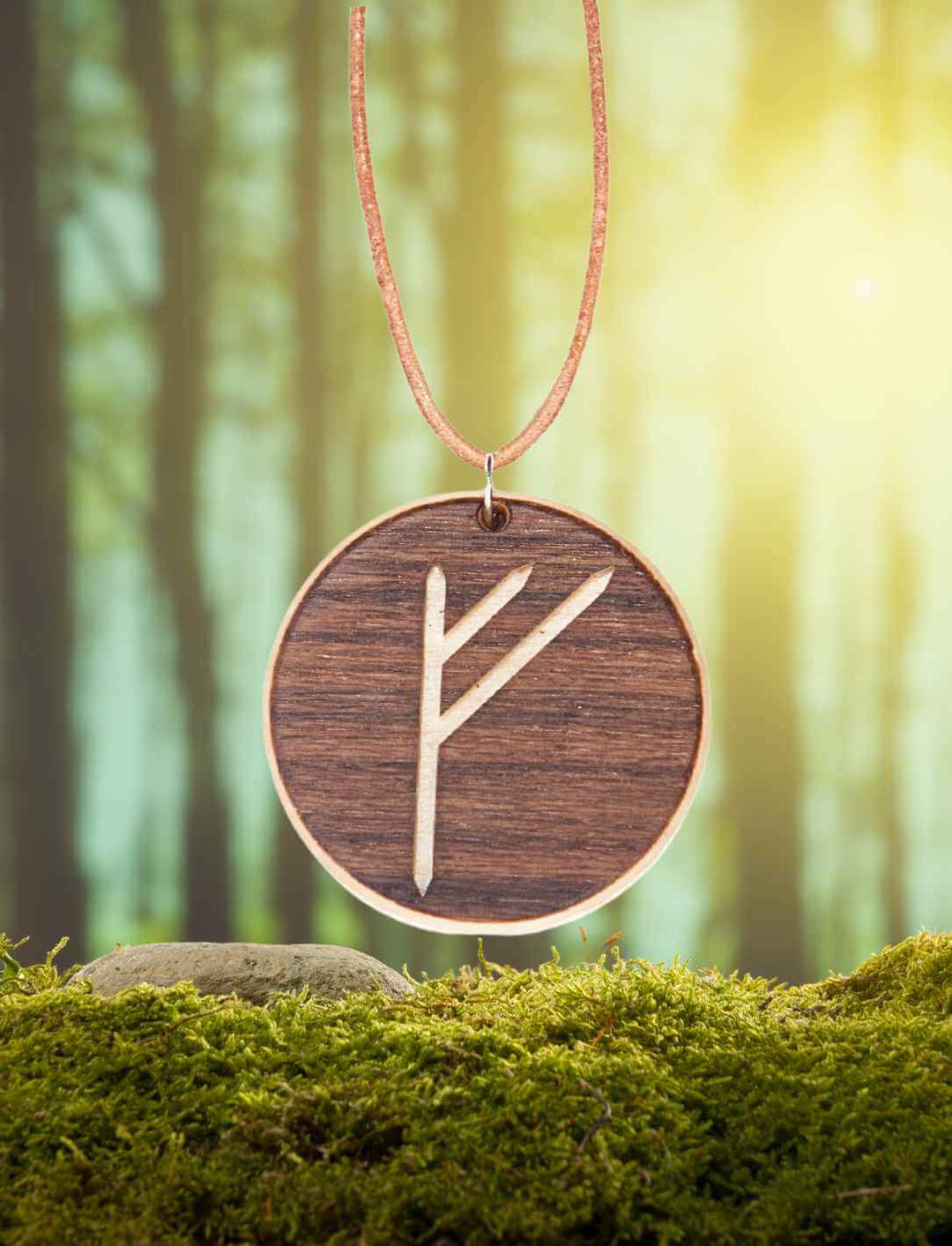 Fehu Rune Amulett aus Ahorn- und Nussbaumholz auf natürlichem Moos/Wald-Hintergrund.