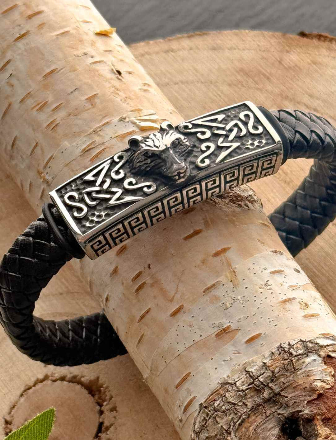 Nordisches Lederarmband Fenrir’s Erbe mit Wolfskopf aus Edelstahl auf geflochtenem Leder, auf Holz fotografiert.