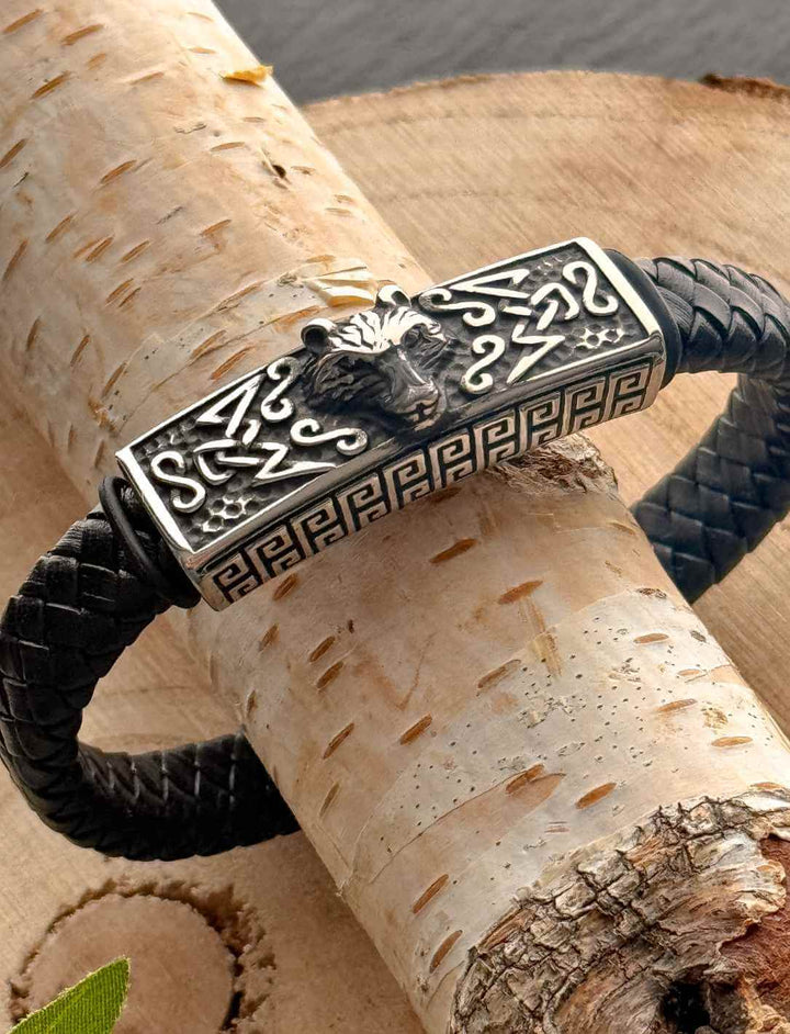 Nordisches Lederarmband Fenrir’s Erbe mit Wolfskopf aus Edelstahl auf geflochtenem Leder, auf Holz fotografiert.