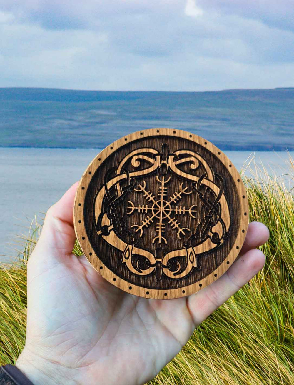 Eichenschatulle mit nordischem Symbol in einer Hand gehalten – Mystik trifft Natur am Rande der Küste.