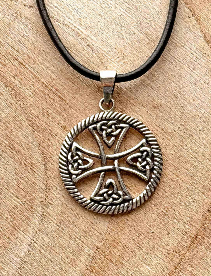 Keltisches Lebensrad – runder Silberanhänger mit Kreuz und keltischen Knoten auf Holzuntergrund mit Lederkordel zum Knoten.