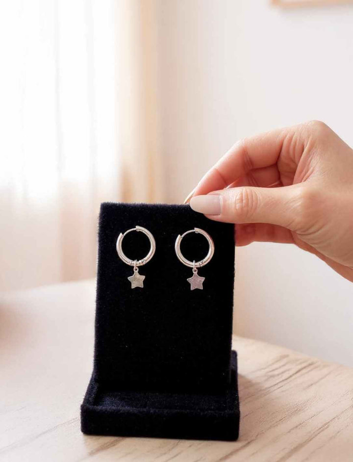 Lunaria Creolen – Edelstahl-Stern-Ohrringe auf schwarzem Display, von Hand präsentiert.