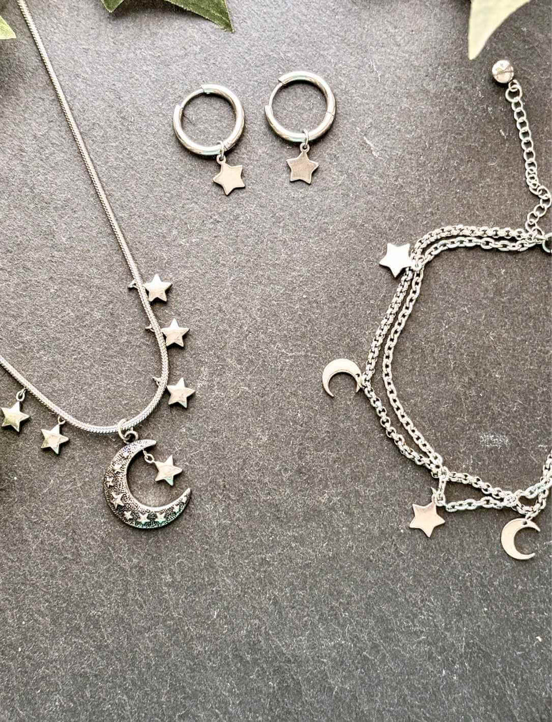 SET: Lunaria Edelstahlkette mit Mond & Sternen – Fantasy Schmuck auf grauem Stein mit Blättern fotografiert. Bestehend aus Halskette, Fusskettchen und Creolen.