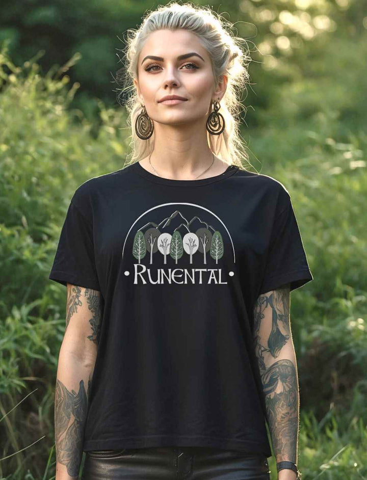 Blonde Frau trägt das schwarze  “Runental Fan-Kollektion” Damen Organic T-Shirt im Wald – Mystisches Design mit Runental-Logo, eingefangen in einer natürlichen Umgebung.
