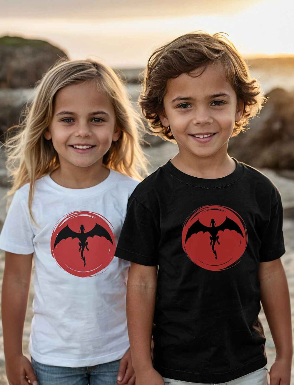 Zwei Kinder am Strand, lächelnd in 'Saga of the Dragon' T-Shirts, das Mädchen in Weiß und der Junge in Schwarz, verkörpern spielerisch den Geist von Abenteuer und Freundschaft.