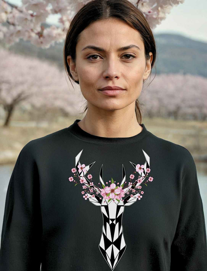 Eine Frau trägt den schwarzen Sakura Deer Organic Unisex Sweater vor einem Hintergrund aus blühenden Kirschblüten, der die japanische Eleganz und Naturverbundenheit widerspiegelt.