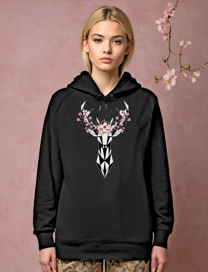 Junge blonde Frau trägt den Sakura Deer organice Unisex Hoodie in schwarz, im Hintergrund ist ein stimmiges Bild mit Kirschblüten.