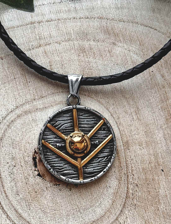 Runenverzierter Titan-Anhänger mit goldfarbener Schildform – Symbol aus der nordischen Mythologie, auf dekorativem Holzhintergrund mit geflochtener Lederkette.
