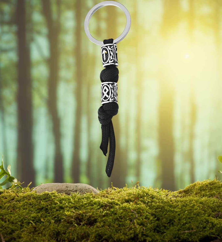 Schlüsselanhänger von Tyr – Paracord-Schlüsselanhänger mit Runenverzierungen aus Edelstahl auf Moos/Wald Hintergrund