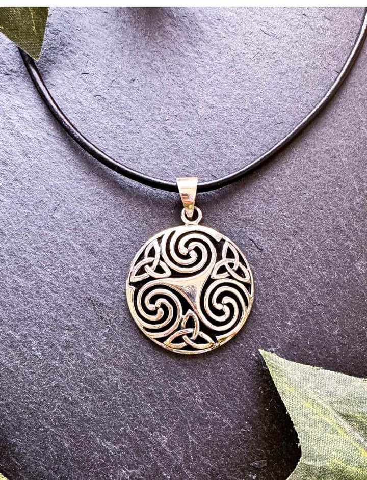 Runder Silberanhänger mit Triskele und Triquetra-Knoten auf dunklem Hintergrund – Symbol für Vergangenheit, Gegenwart und Zukunft
