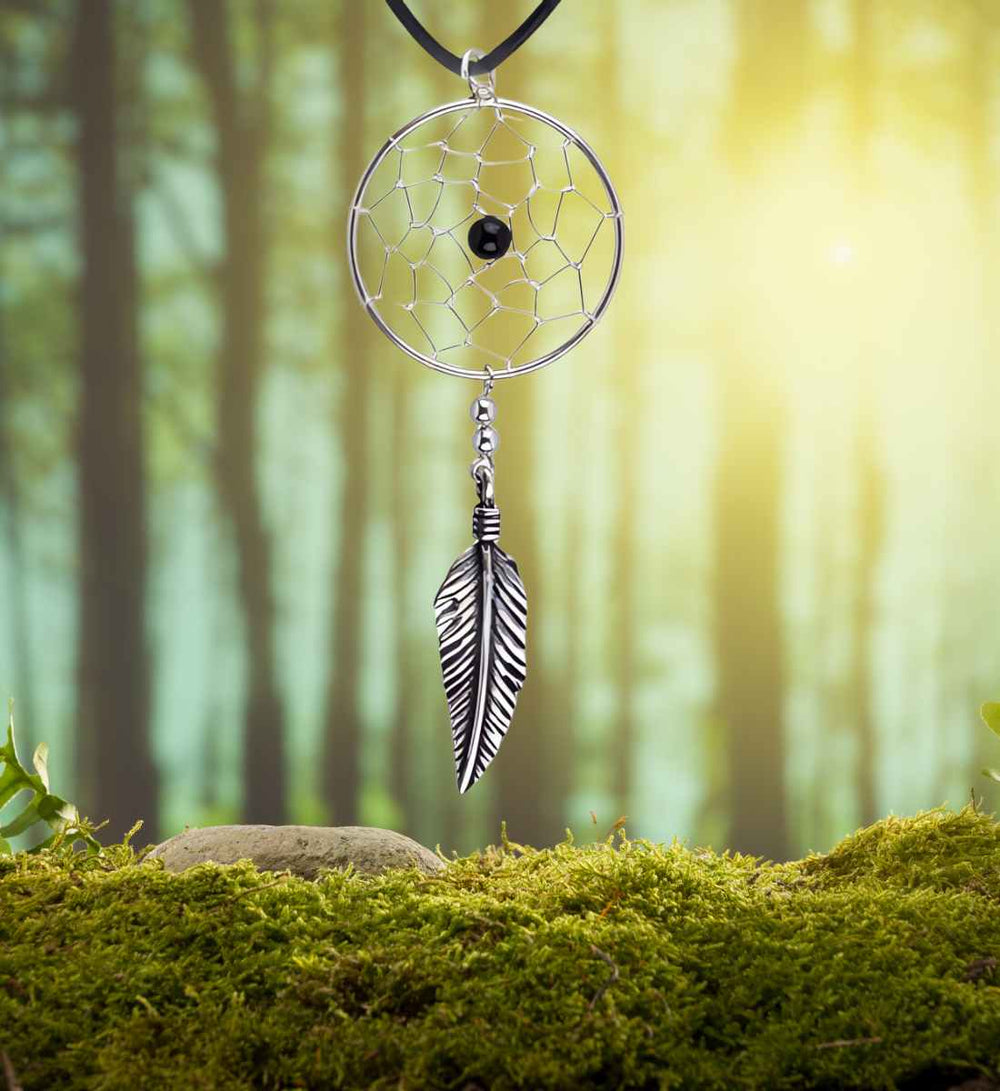 Traumfänger der silbernen Feder mit Onyx, umgeben von der ruhigen Atmosphäre eines Waldes, spiegelt die Verbindung mit der Natur und alten Traditionen wider.