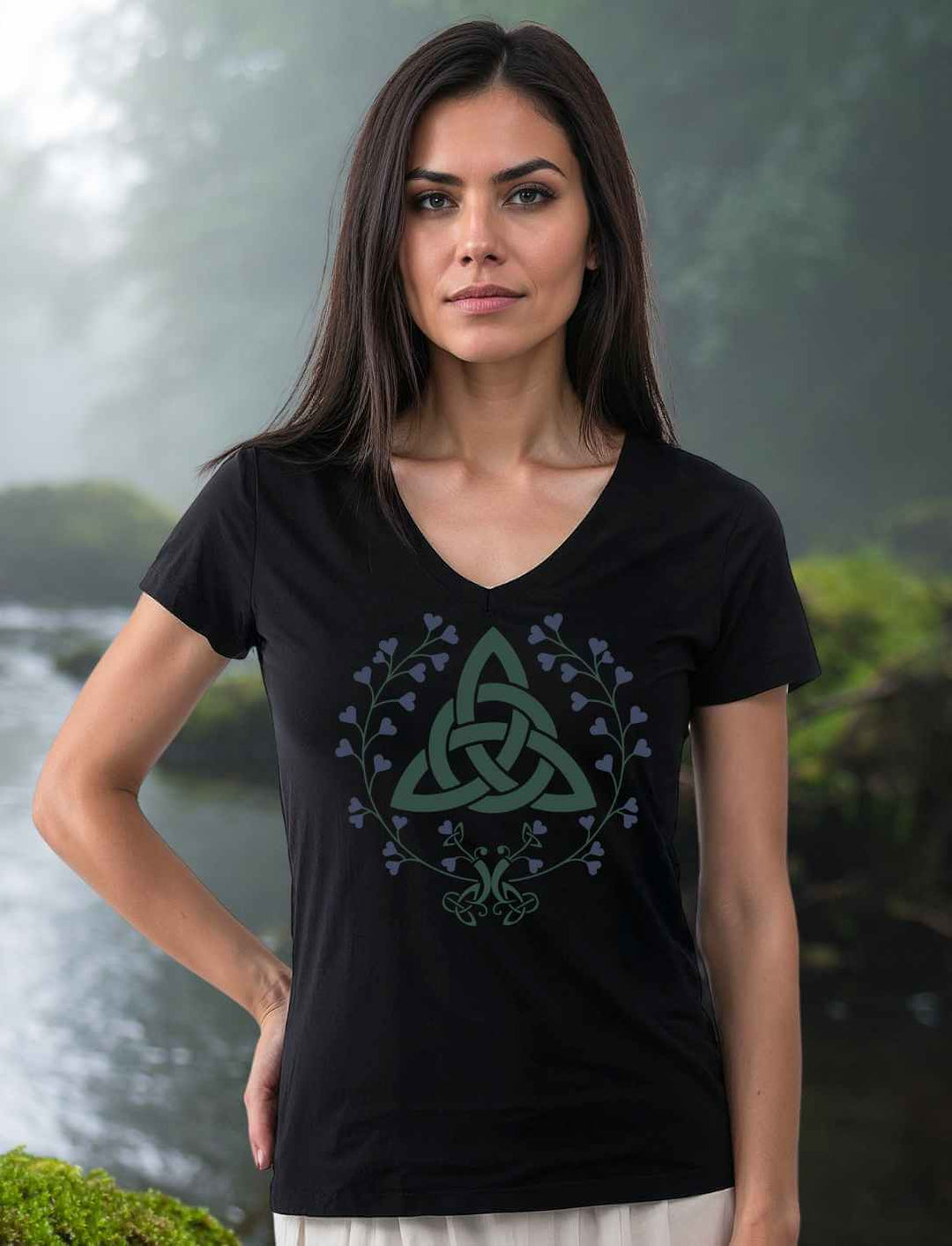 Model trägt das Damen V-Neck-Shirt „Triquetra des grünen Bundes“ in Schwarz, stehend an einem ruhigen Bachlauf mit moosbedecktem Ufer – harmonisches Zusammenspiel aus Natur und Symbolik.