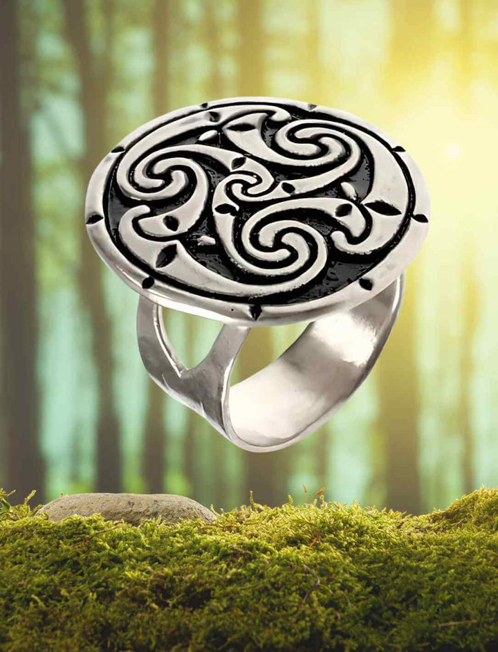Der „Triskelion der Göttin Brigid“ Ring schwebt vor einer Waldszene – das keltische Triskelion-Symbol leuchtet in silbernem Glanz und verkörpert den ewigen Wandel.