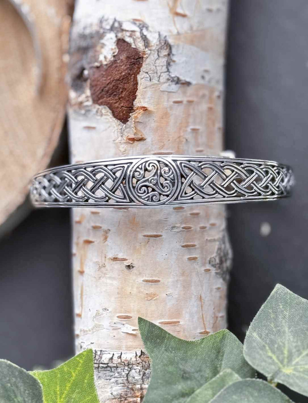 Keltischer Armreif aus 925 Silber mit Triskelion und Knotenmuster, frontal fotografiert auf Birkenrinde.