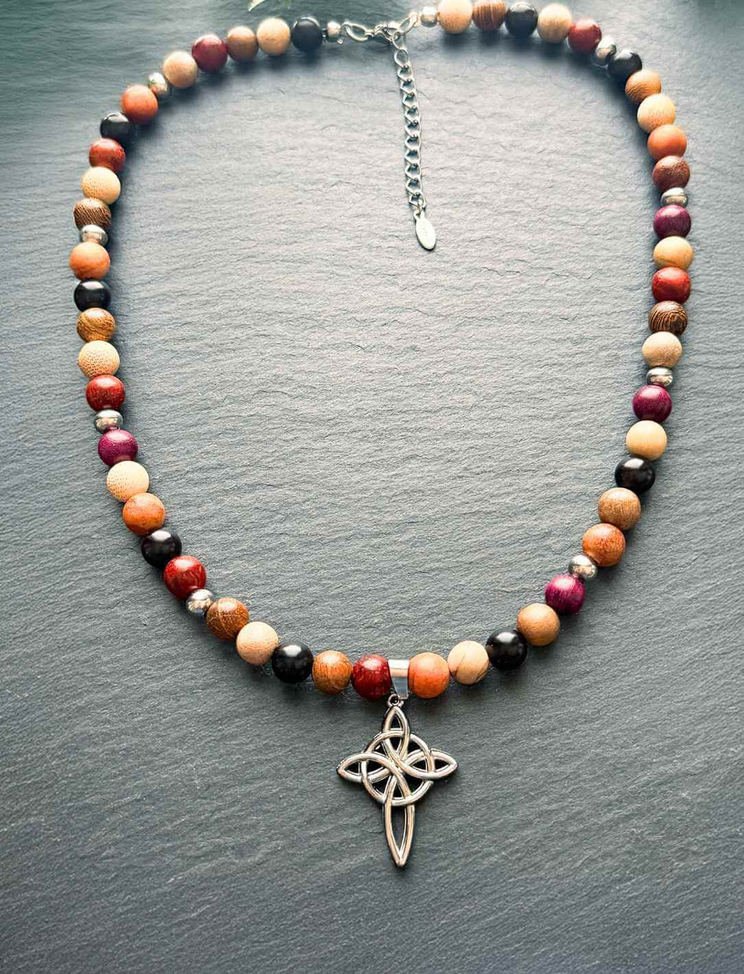 „Wächterin des Hains“ – keltische Holzperlenkette mit Edelstahlanhänger, arrangiert auf dunkler Steinoberfläche.