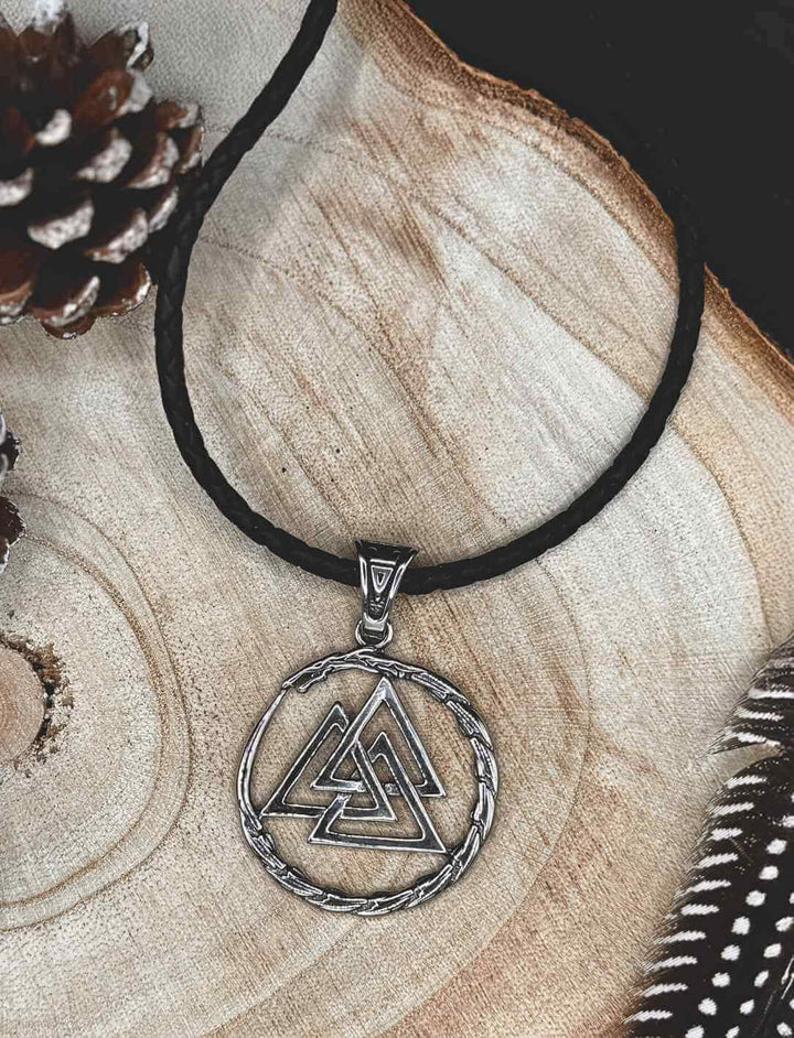 Weltenring der Midgardschlange – Edelstahlanhänger mit Valknut-Symbol, kombiniert mit schwarzer, geflochtener Lederkette, dargestellt auf einem rustikalen Holzuntergrund