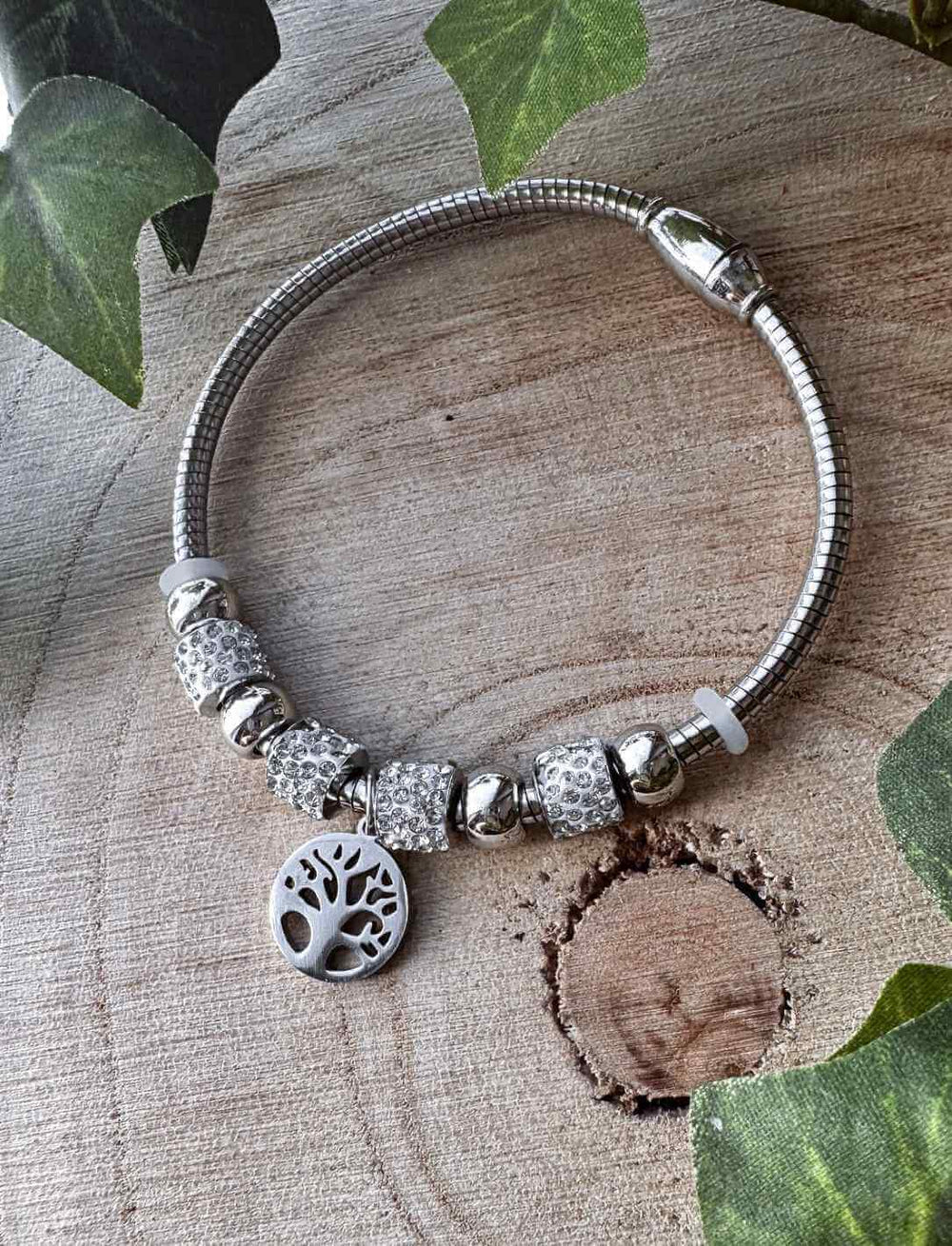 Edelstahlarmband „Yggdrasils Glanz“ mit funkelnden Kristallen und Lebensbaum-Symbol, stimmungsvoll präsentiert auf Holz