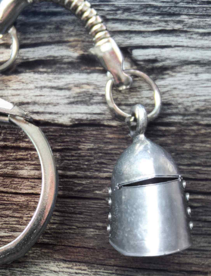 Schlüsselanhänger mit Ritterhelm aus Zinn, Symbol für Mut und Schutz, vor einem Holz Hintergrund.