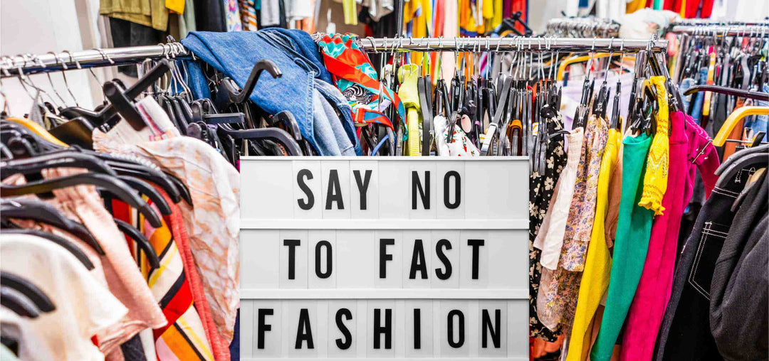 Kleiderstangen voller bunter Kleidung mit einem Schild in der Mitte, auf dem 'Say No to Fast Fashion' steht.