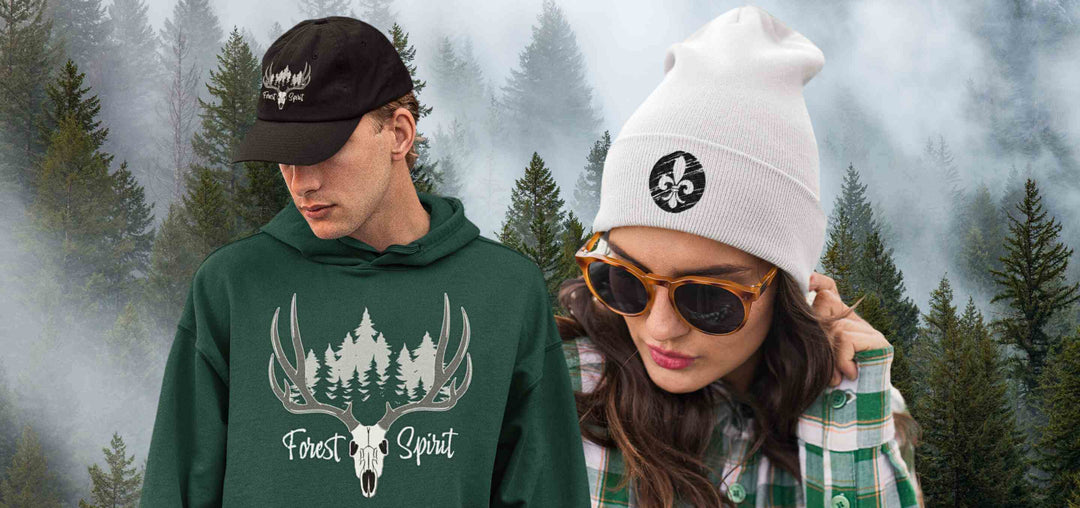 Ein Mann trägt eine schwarze Cap mit mystischem Wald-Design, daneben eine Frau mit weißer Beanie und Lilien-Symbol. Beide stehen vor einem nebligen Wald, perfekt gestylt für Naturliebhaber und Fantasy-Fans. Runental.de