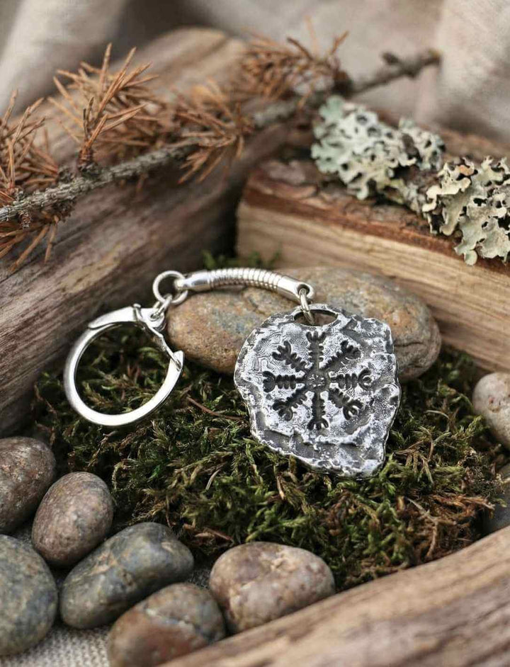 Aegishjálmur Schlüsselanhänger aus Zink mit isländischem Runenkreis, liegend auf Moos, Holz und Natursteinen