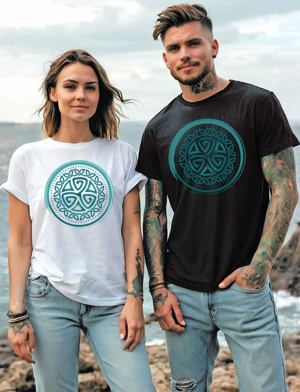 Junge Frau und junger Mann tragen das Aqua Triskele Knoten Shirt, die Frau in Weiß und der Mann in Schwarz. Sie stehen an einer felsigen Küste
