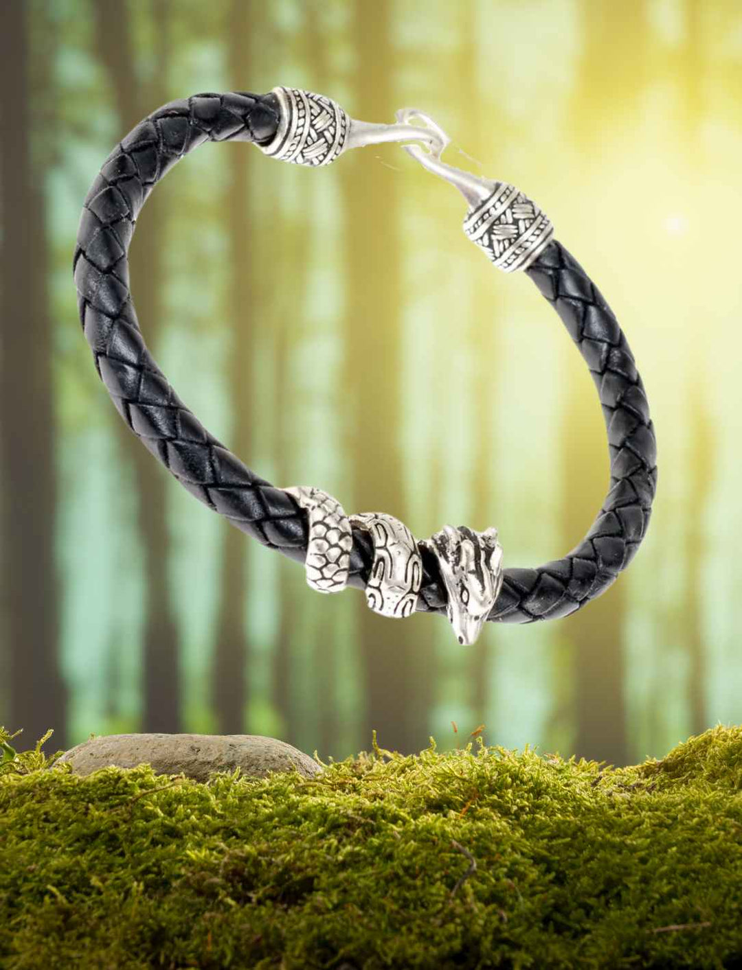 Armband des Drachens aus Leder mit versilbertem Drachenkopf, präsentiert auf Moos in einem Waldhintergrund.