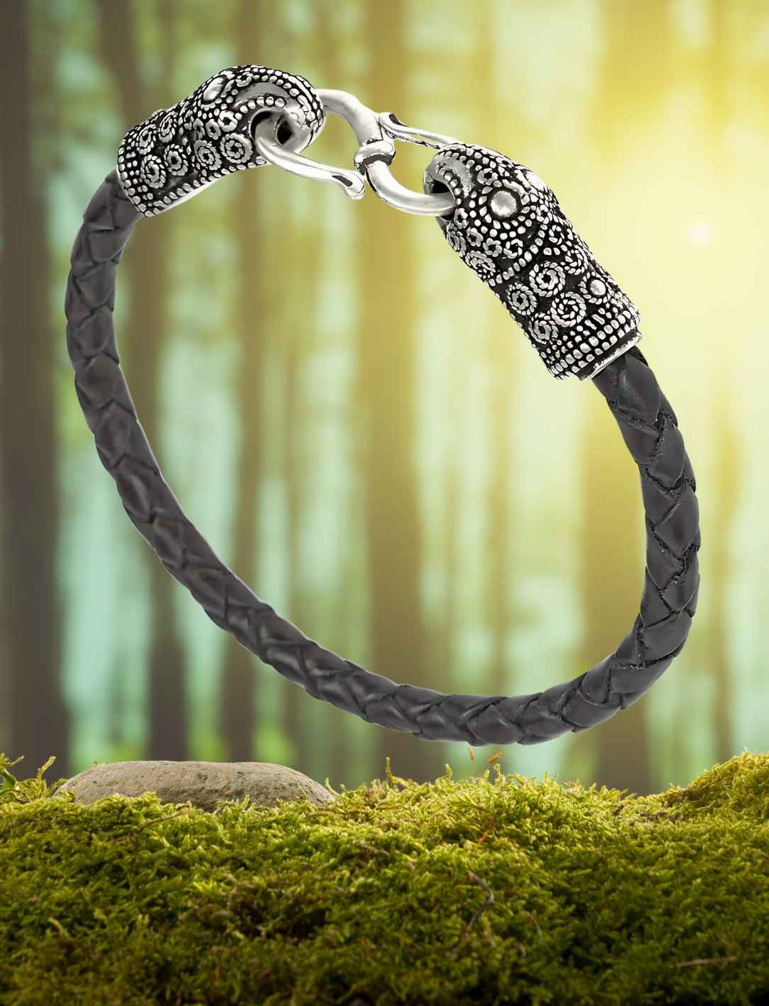 Schwarzes Lederarmband des Rabenwächters mit silbernen Rabenköpfen auf Wald/Moos Hintergrund.