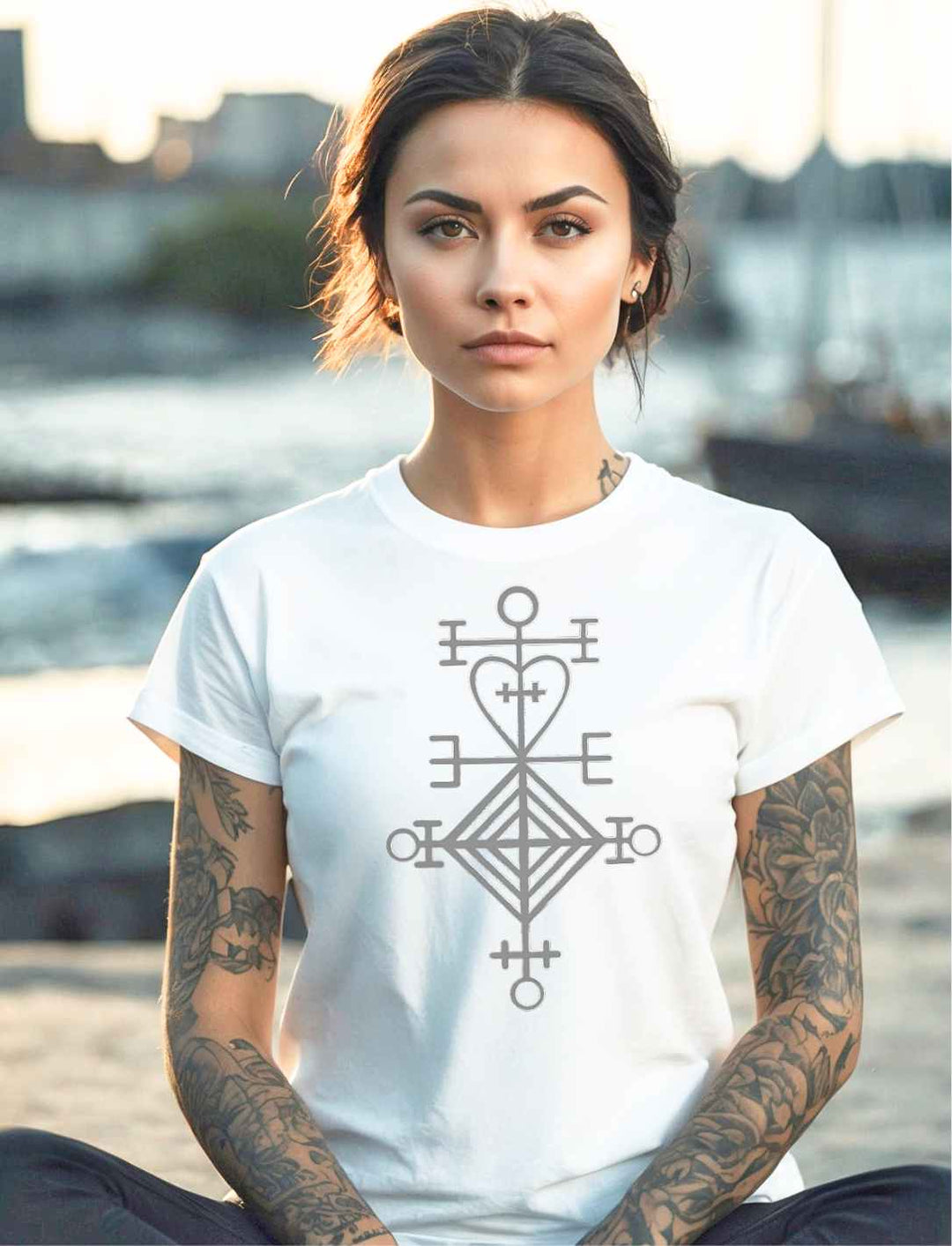 Junge Frau trägt ein weisses Astarstafur Damen T-Shirt mit isländischen Symbol für Liebe und Schutz, am Hafen sitzend – kraftvolles Design, inspiriert von nordischer Tradition.