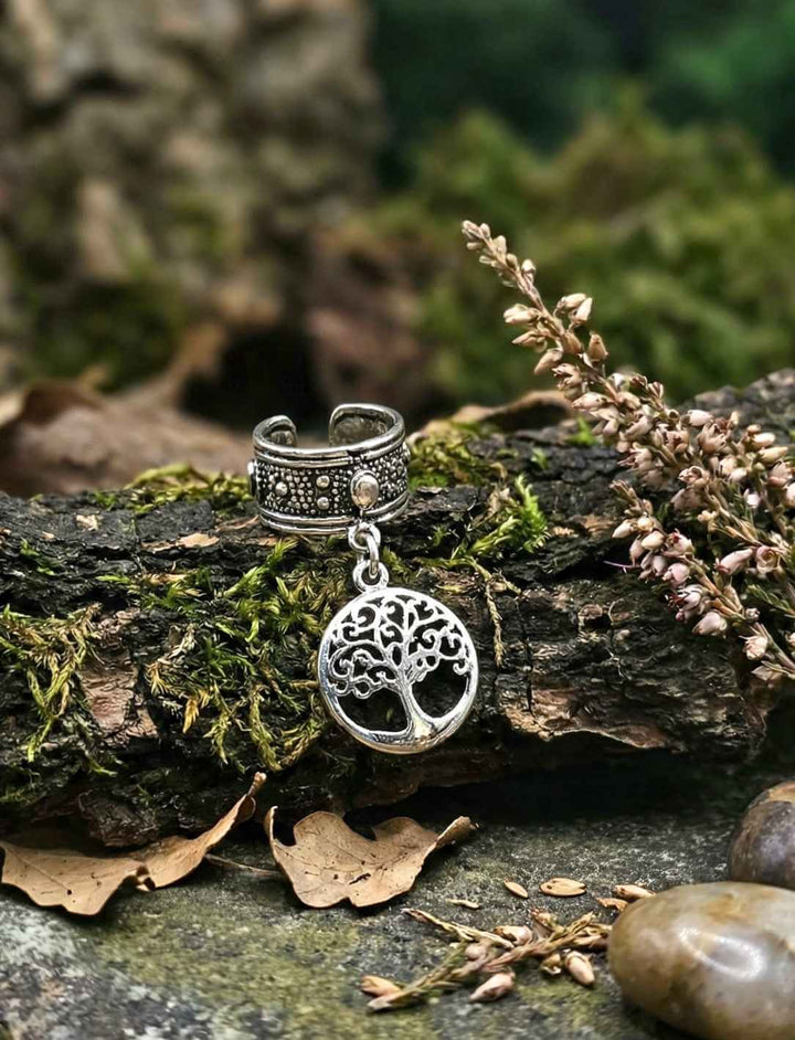 Silberner Lebensbaum-Anhänger auf bemooster Rinde mit Heidekraut und Steinen – Natur-Fotografie