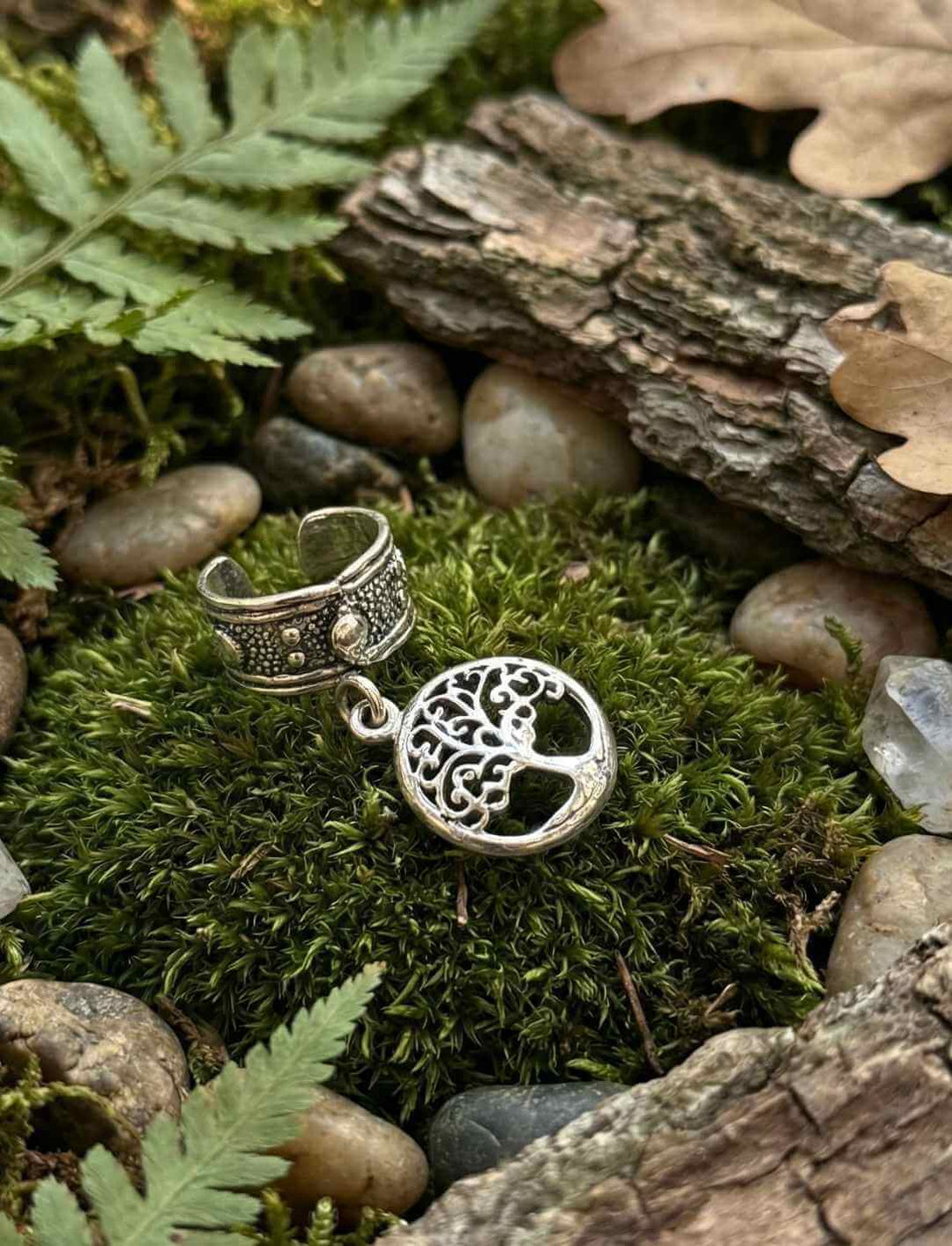 Lebensbaum-Anhänger aus Silber auf Moos zwischen Steinen und Farn im Wald-Setting