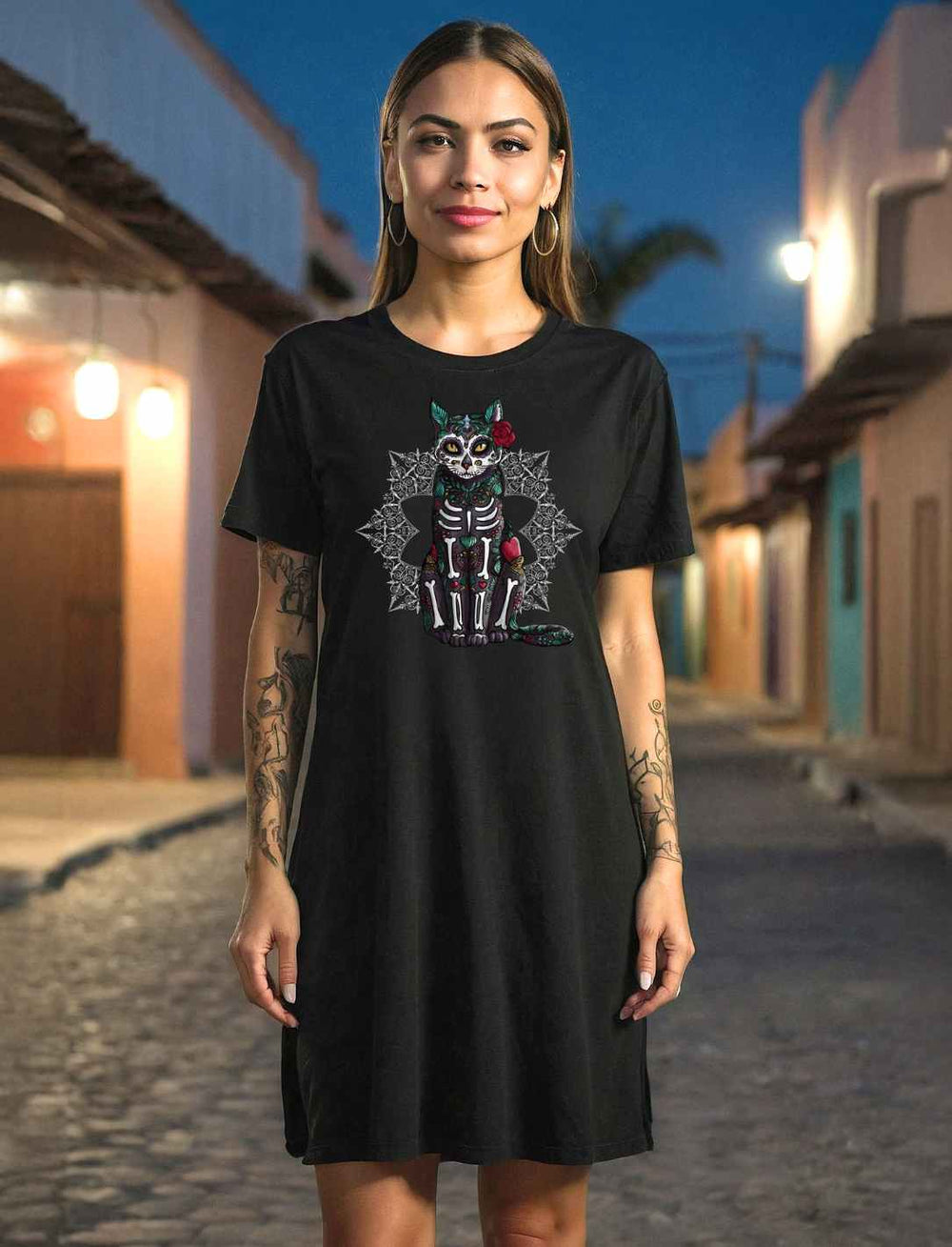 Frau trägt ein „Catrina Felina“ T-Shirt Kleid in Schwarz von Runental.de. Mystisches Design mit Katzenmotiv inspiriert vom Día de los Muertos, im Abendlicht auf einer gepflasterten Straße abgebildet.